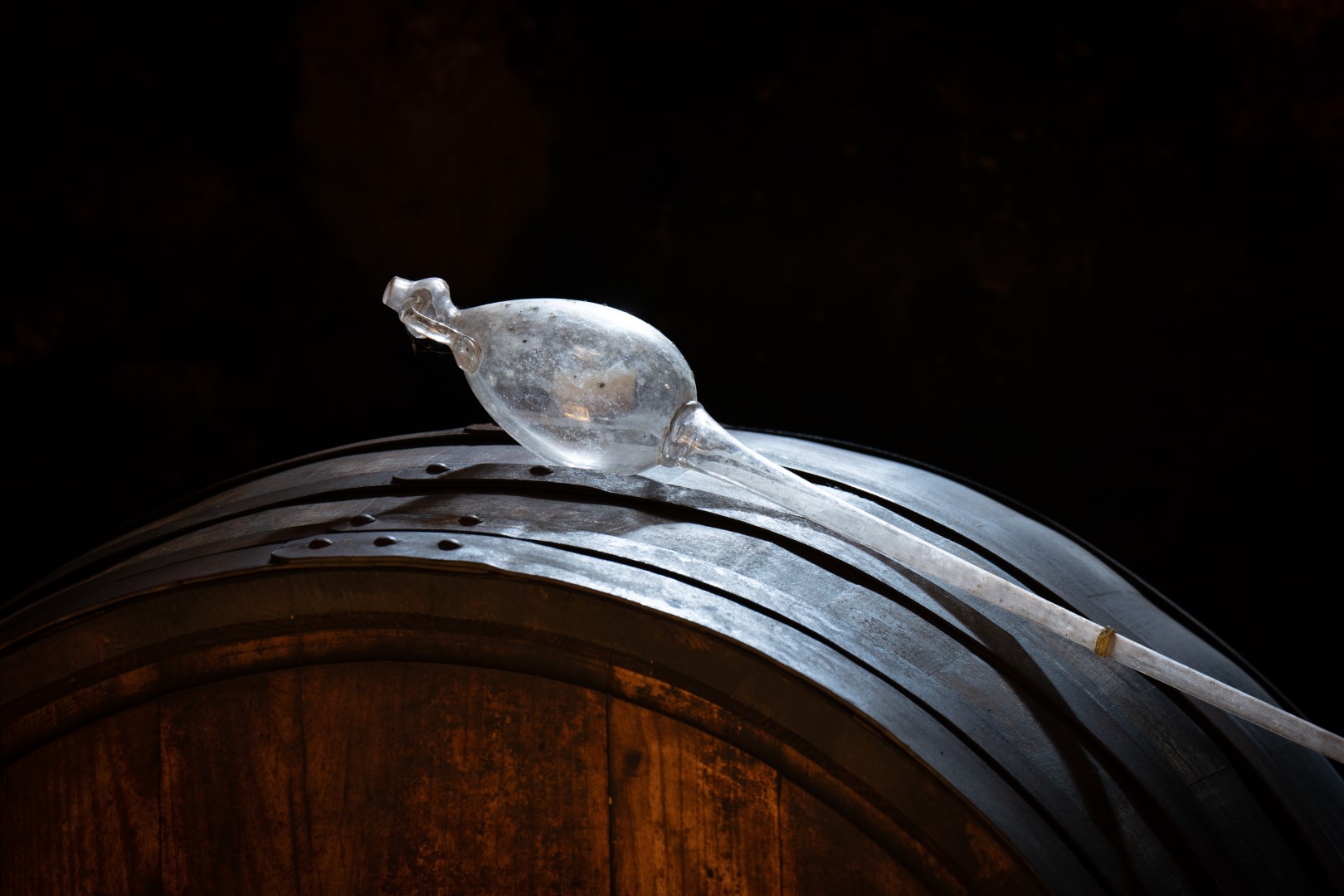 Eine traditionelle Glas-Pipette liegt auf einem alten Weinfass in einem dunklen Keller, hervorgehoben durch ein Lichtstrahl.