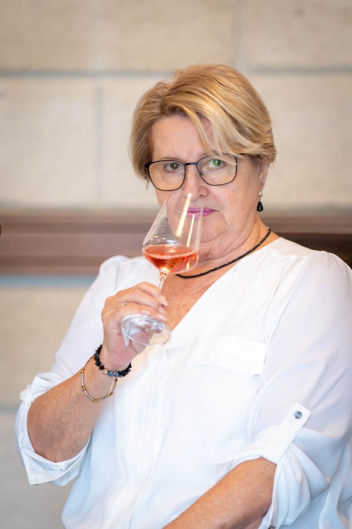 Eine elegante Dame mit Brille genießt ein Glas Roséwein, ihr Blick voller Wertschätzung für den Tropfen.